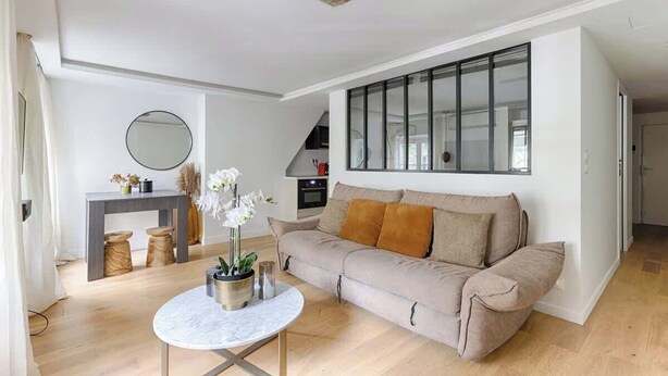 Ein stilvolles Wohnzimmer mit einem beigefarbenen Sofa, einem runden Couchtisch und einem großen Fenster mit Jalousien.