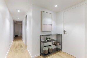 Un pasillo con suelo de madera, una puerta blanca, un espejo en marco y una consola metálica con adornos.