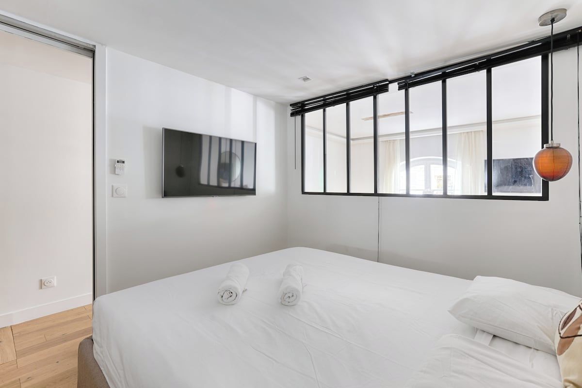 Een moderne hotelkamer met een bed, een aan de muur bevestigde televisie en een raam met zonwering.