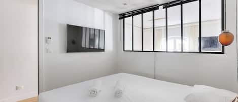Een moderne hotelkamer met een bed, een aan de muur bevestigde televisie en een raam met zonwering.