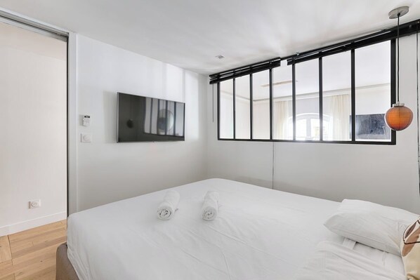 A modern hotel room with a bed, a television mounted on the wall, and a window with blinds.