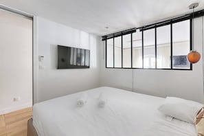 Et moderne hotelværelse med seng, tv ophængt på væggen og et vindue med persienner.