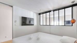 Ein modernes Hotelzimmer mit einem großen Bett, einem flachbildfernseher an der Wand und einem Fenster mit Jalousien.