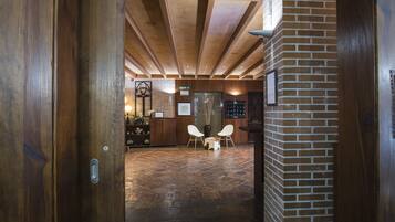 Un área de recepción con un mostrador de madera, dos sillas blancas, piso de baldosas y pared de ladrillo.