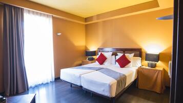 A hotel room with a double bed, two bedside tables with lamps, a wooden headboard, and a large window with curtains.