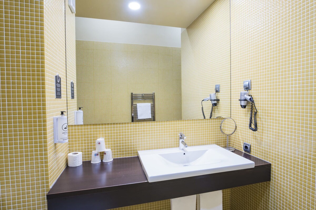 A bathroom with yellow-tiled walls, a white sink, a towel rack, and a hairdryer.