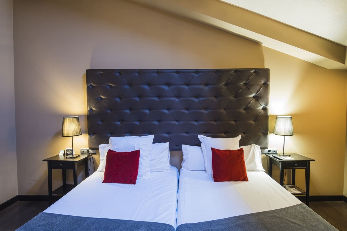 Una camera d'albergo con un letto grande, due comodini e una testiera imbottita.