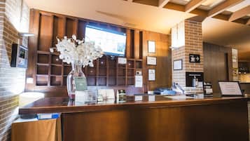 Un mostrador de recepción con encimera de madera, un jarrón con flores blancas, una pantalla digital y un cartel de Wi-Fi.