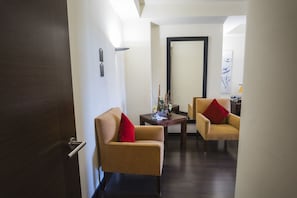 A hotel room with a wooden door, two beige armchairs with red cushions, a small wooden table with decorative items, and a large mirror on the wall. - Alda Castillo De Olite (Olite)