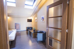 A hotel room with a bed, a desk, a chair, a small table, and a potted plant. There is a wooden door with frosted glass panels and a skylight above the bed. - Alda Castillo De Olite (Olite)