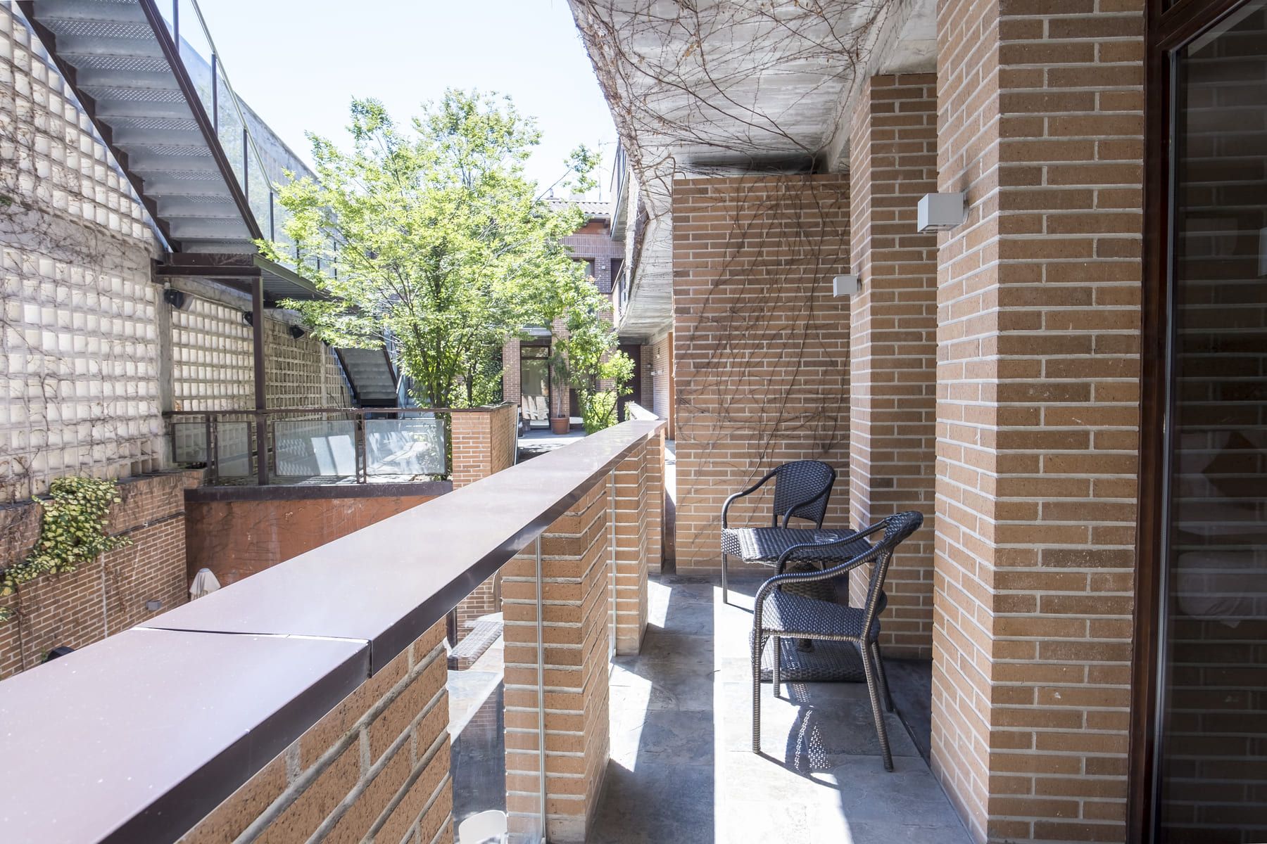 A balcony with brick walls, a metal railing, and two wicker chairs.