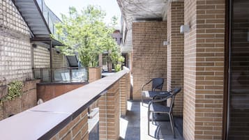 A balcony with brick walls, a metal railing, and two wicker chairs.