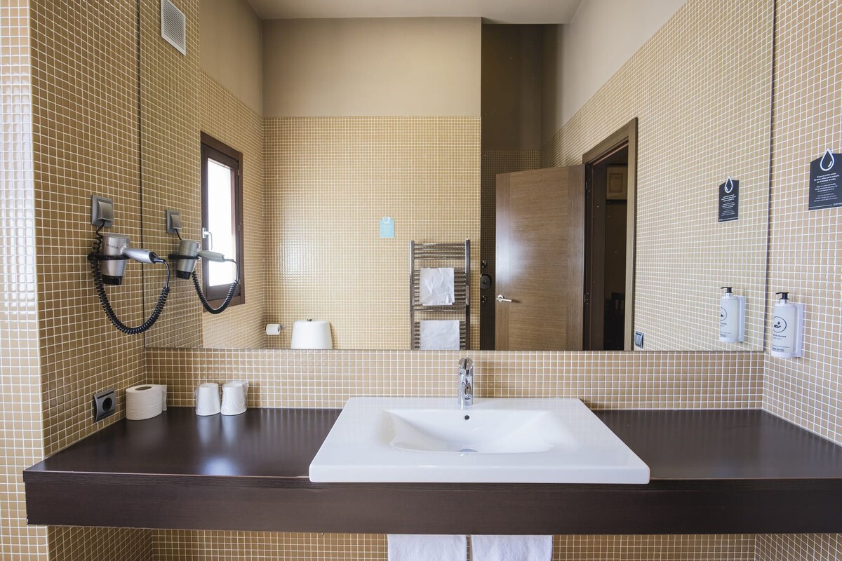 Un baño con un espejo grande, un lavabo y un secador de pelo montado en la pared.