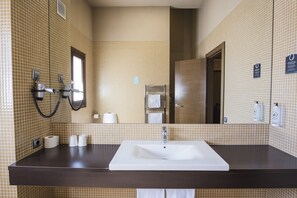 A bathroom with a large mirror, a sink, and a hairdryer mounted on the wall. - Alda Castillo De Olite (Olite)