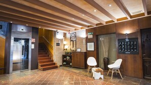 Vestíbulo de hotel con escalera, mostrador de recepción y zona de estar.
