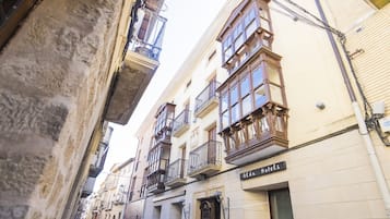 Une rue étroite bordée d’immeubles dotés de balcons et d’une enseigne indiquant « Alda Hotels ».