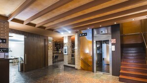 Un vestíbulo de hotel con suelo de baldosas de piedra, un mostrador de recepción, una zona de bar y una escalera.
