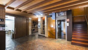 A hotel lobby with a stone-tiled floor, a reception desk, a bar area, and a staircase.