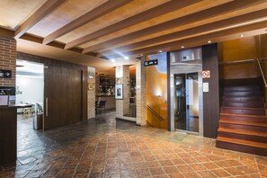 Un vestíbulo de hotel con suelo de baldosas de piedra, un mostrador de recepción, una zona de bar y una escalera.