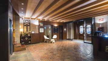 A lobby with a wooden ceiling, brick walls, a reception desk, two white chairs, and a tiled floor.