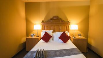Habitación de hotel con una cama grande, dos mesitas de noche, dos lámparas y un cabecero de madera.