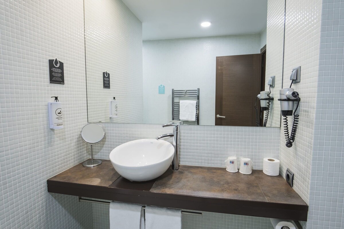 A modern bathroom with a large sink, a mirror, a towel rack, and a hairdryer.