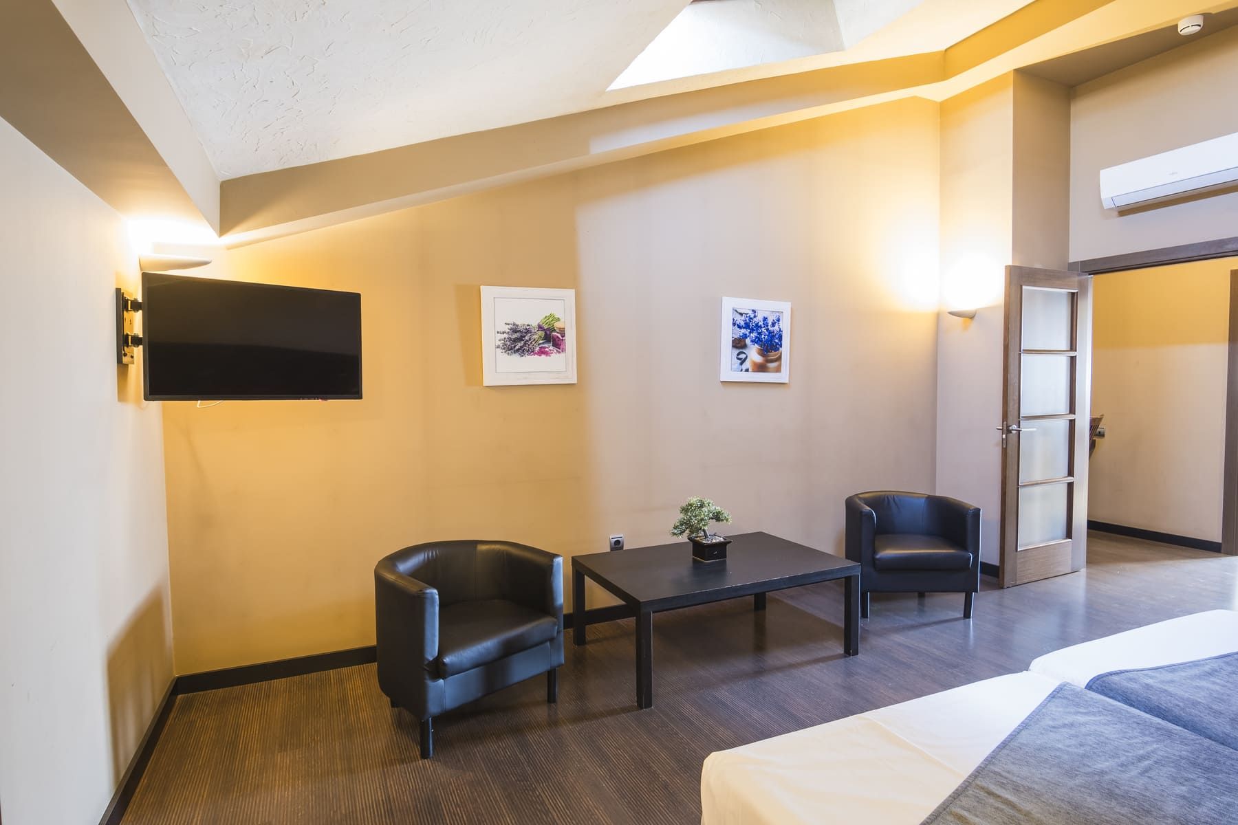 A hotel room with a bed, two black leather chairs, a small table, and a potted plant.