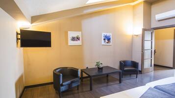 A hotel room with a bed, two black leather chairs, a small table, and a potted plant.