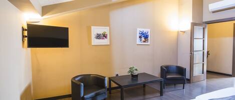 A hotel room with a bed, two black leather chairs, a small table, and a potted plant.