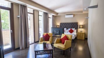 Habitación de hotel con cama, televisión, escritorio, dos sillas y ventana con cortinas.