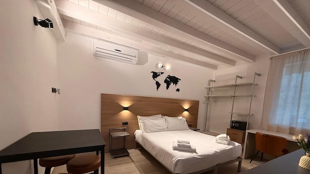 Een moderne hotelkamer met een houten hoofdeinde, een bed met witte lakens, een bureau met stoel, en een zithoek met krukken.