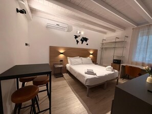 A modern hotel room with a wooden headboard, a bed with white linens, a desk with a chair, and a small seating area with stools. - 5 Terre hub suite (La Spezia)