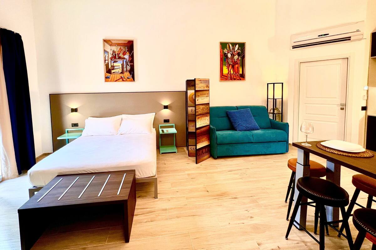 Une chambre d’hôtel comprenant un lit, un bureau avec deux chaises, un canapé, une table de chevet et deux lampes fixées au mur.