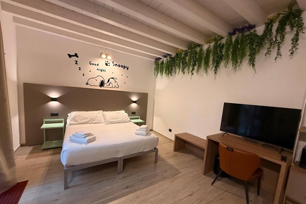 Une chambre moderne avec un lit, des tables de chevet, une télévision et un mur décoré avec des motifs de Snoopy.