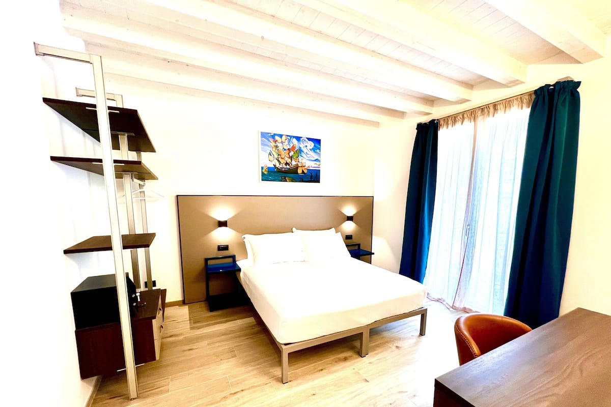Une chambre d’hôtel avec un lit, des tables de chevet, un bureau, une chaise et un tableau au mur.