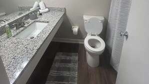 A bathroom with a granite sink, toilet, and a shower curtain.