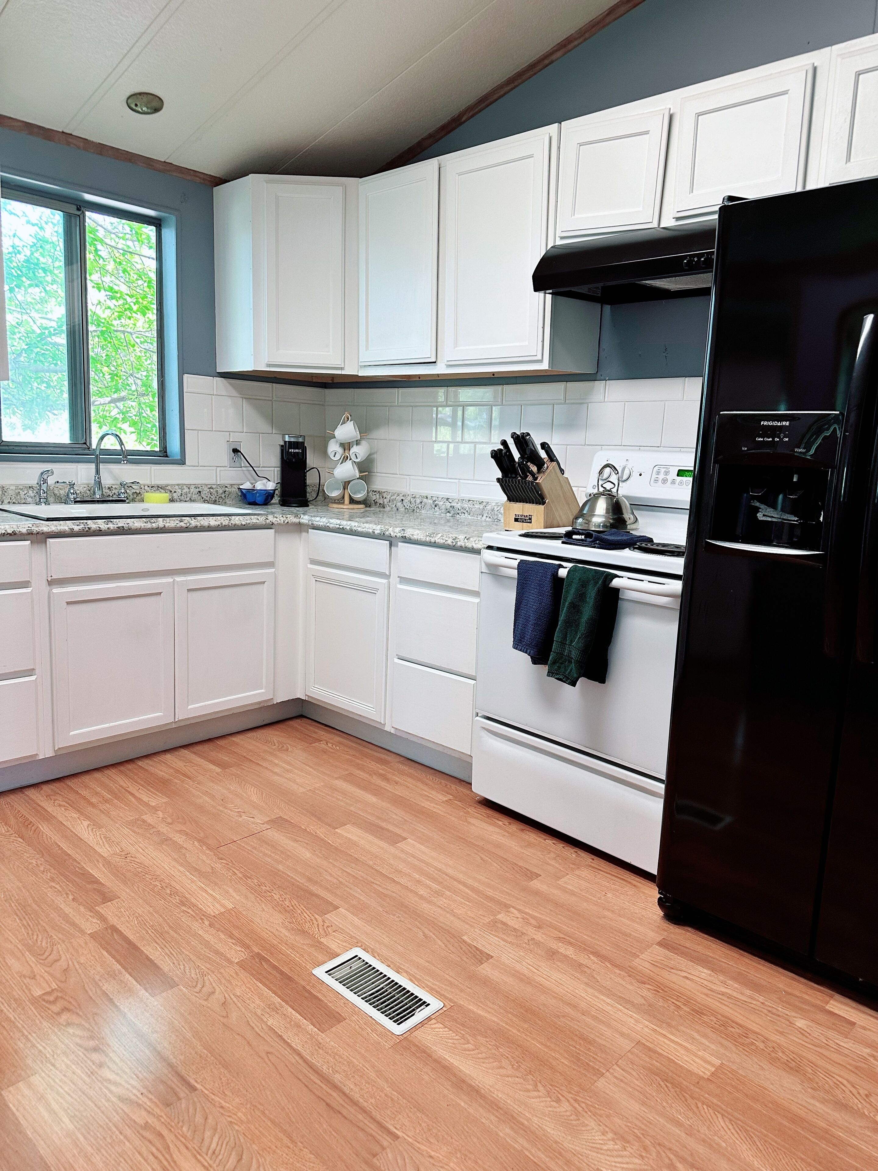 A modern kitchen with white cabinets, a black refrigerator, and a window providing natural light.