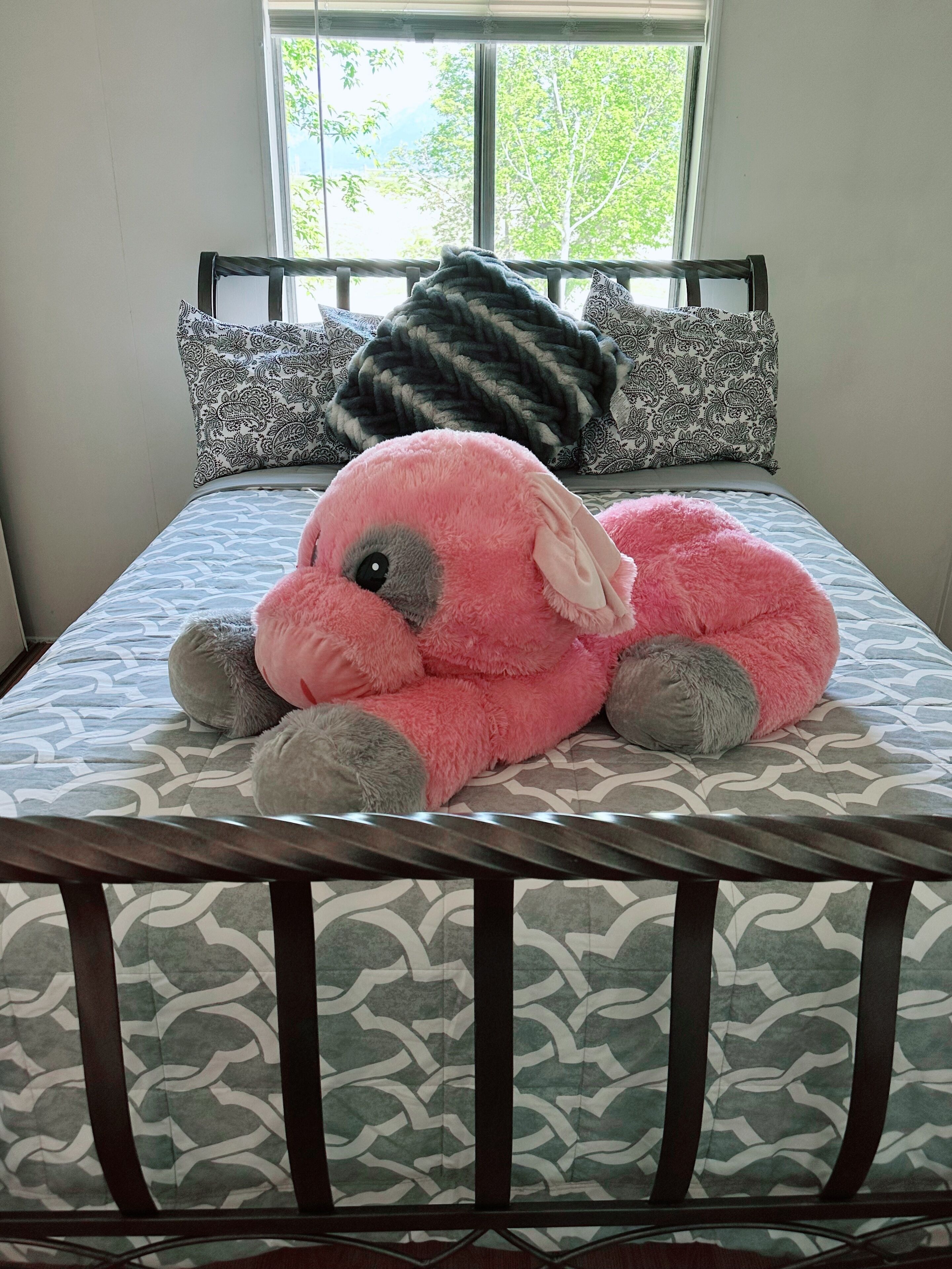 Ein Bett mit einem gemusterten Überwurf, einem großen rosa Kuscheltier und gemusterten Kissen.