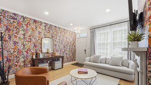 Ein Wohnzimmer mit floraler Tapete, einem Sofa, einem Couchtisch und einem an der Wand befestigten Fernseher.