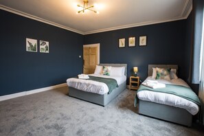A bedroom with two beds, a wooden door, and framed pictures on the wall. - Arbeia in South Shields (South Shields)