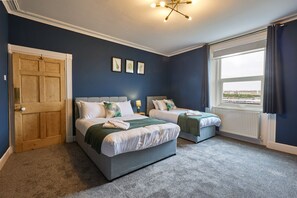 Une chambre avec deux lits, une porte en bois, une fenêtre avec des rideaux et une vue sur l’extérieur.