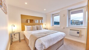 Een moderne hotelkamer met een groot bed, bedlampjes, een houten hoofdeinde, uitzicht op de stad door een raam en een radiator.