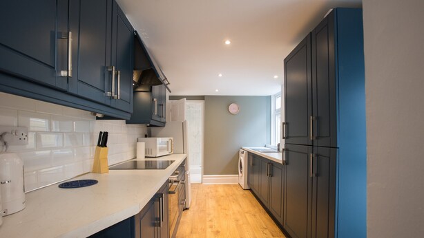 A modern kitchen with dark blue cabinets, a white countertop, and a wooden floor.