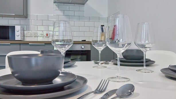 Una mesa de comedor lista con platos, tazones, cubiertos y copas de vino.