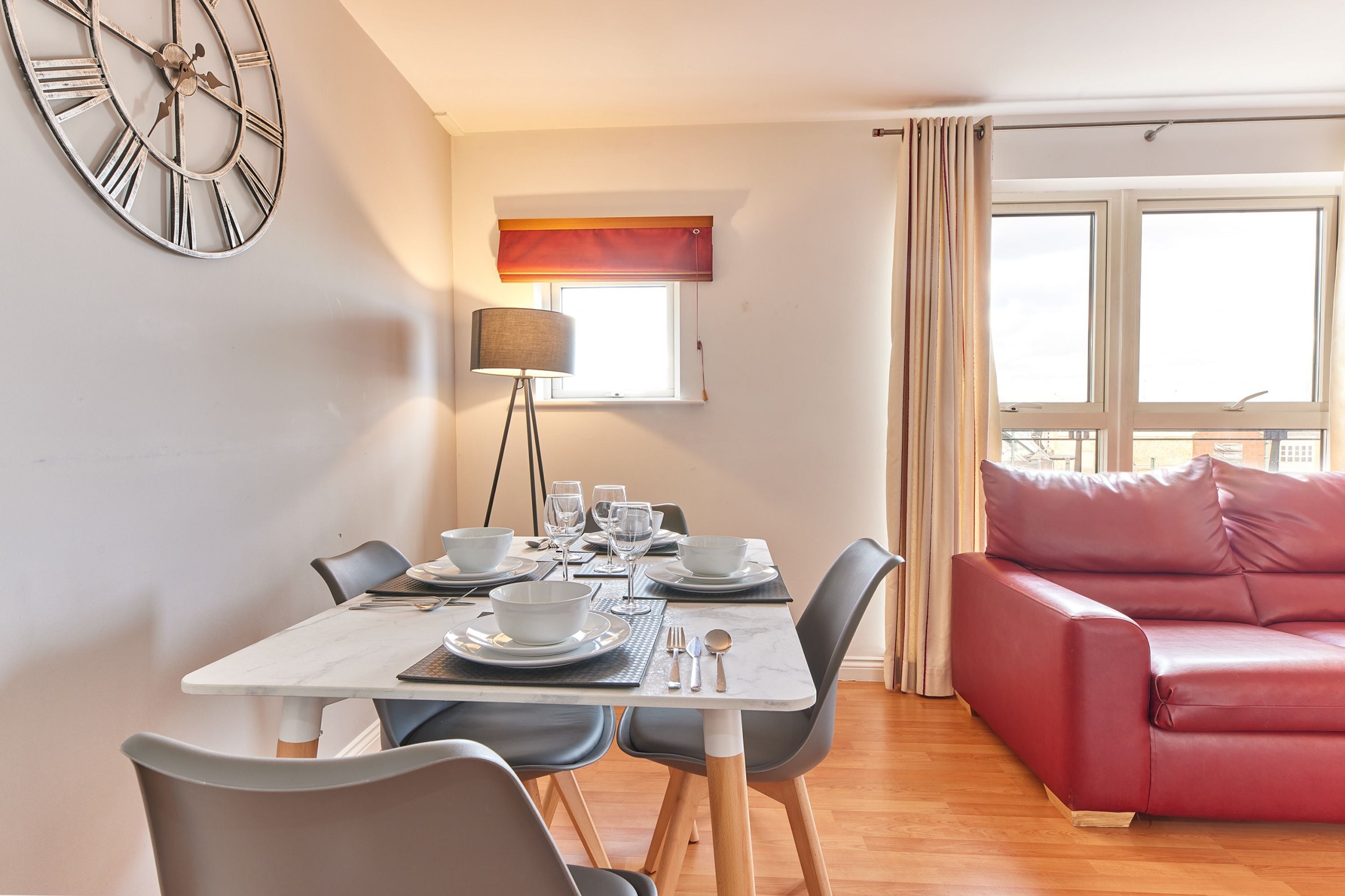 A dining area with a table set for four, a red sofa, and a wall clock.