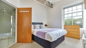 A bedroom with a bed, a wooden door, a window, and a shower area. - The Loft in Newcastle Upon Tyne (Newcastle-upon-Tyne)