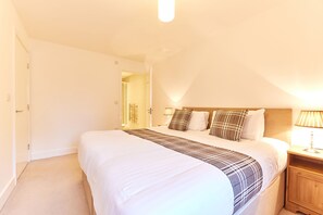 A neatly made bed with a plaid throw blanket, a bedside lamp, and a wooden nightstand. - Willow in Newcastle With 2 Bedrooms and 2 Bathrooms (Newcastle-upon-Tyne)