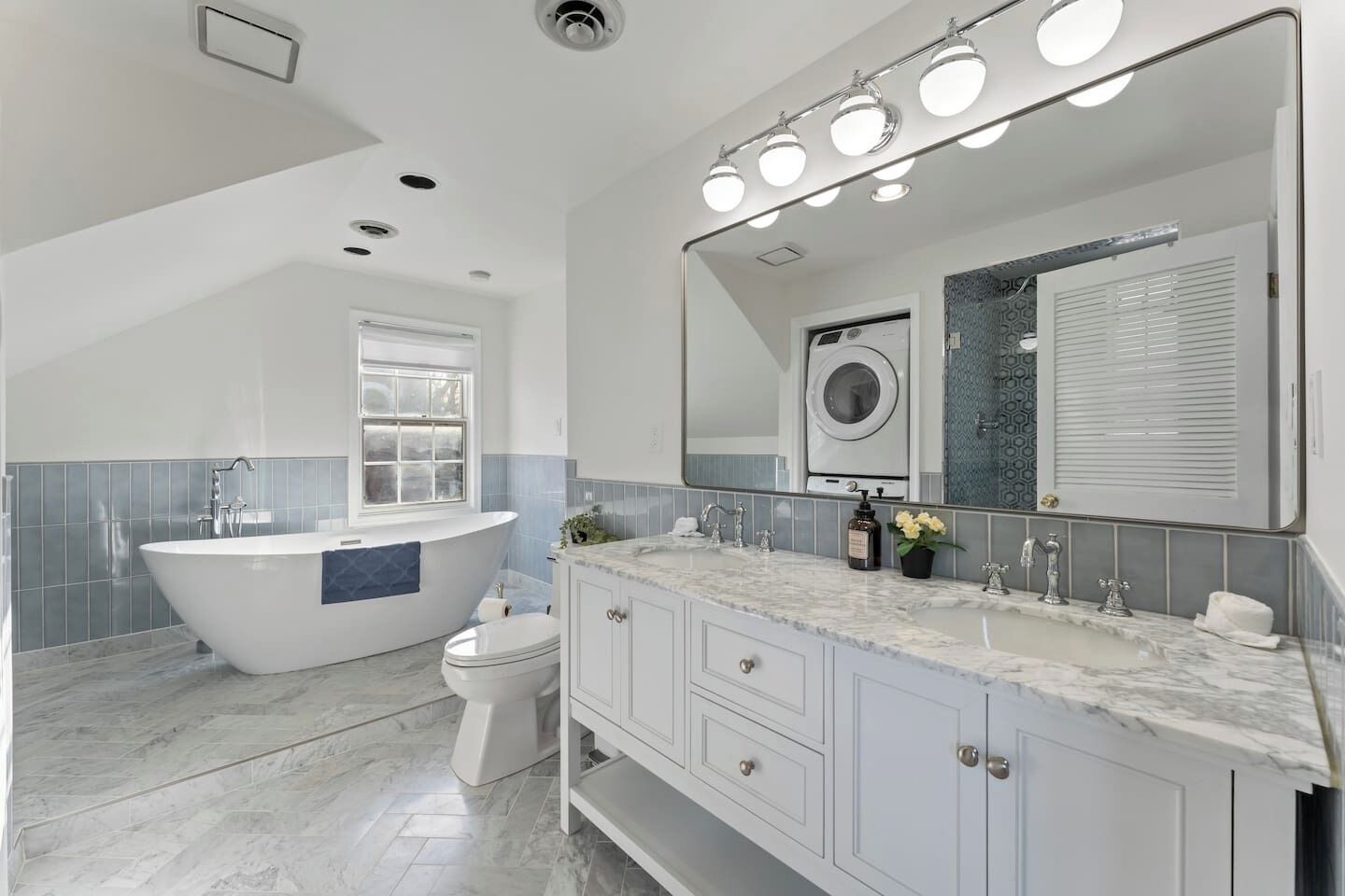 Un bagno moderno con una vasca da bagno indipendente, un water, un mobile lavabo con uno specchio grande e una lavatrice.