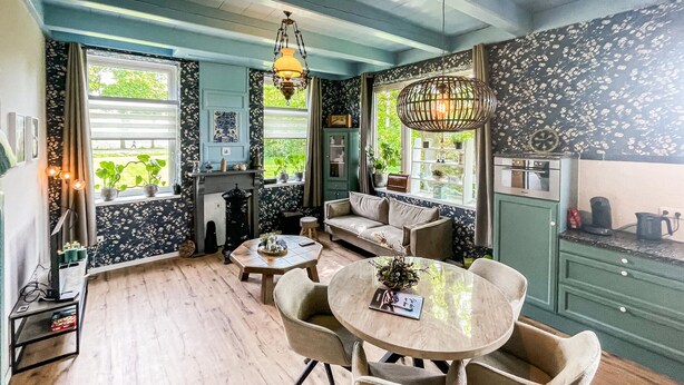 A cozy room with a wooden floor, a round table with chairs, a sofa, and a kitchen area with a stove and cabinets. - Cozy home in Harich with WiFi (Harich)