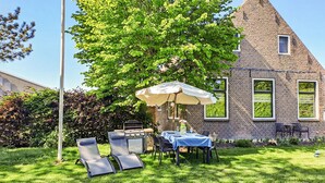 An outdoor patio with a grill, lounge chairs, and a table set for dining, surrounded by a brick building and greenery. - Cozy home in Harich with WiFi (Harich)